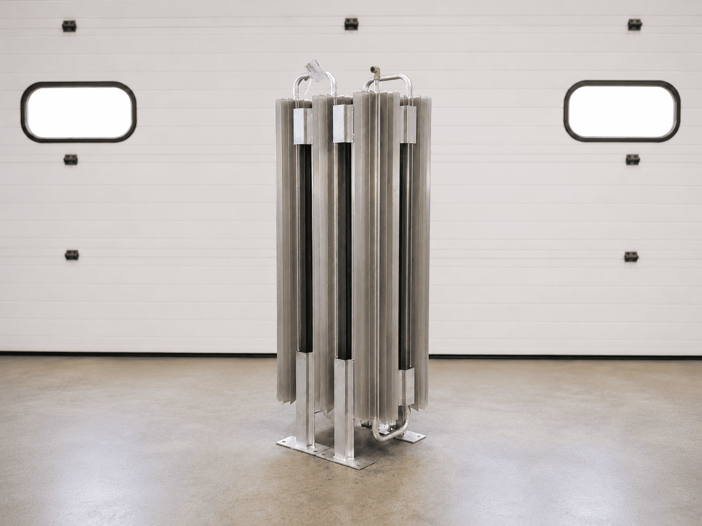 An FWM DVAP dewar-style finned-aluminum vaporizer standing on its bolt-down skid in front of a white facility door